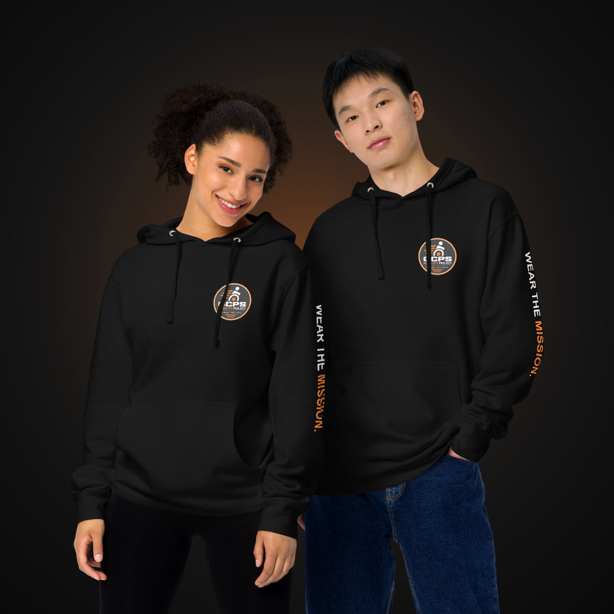 Two people wearing the black GCPS Mobility Project Hoodie, showing the chest badge and "Wear the Mission" sleeve print