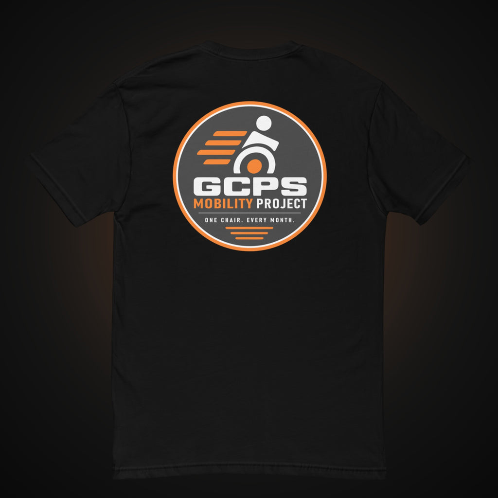 Back of the black GCPS Mobility Project T-Shirt with a large orange, gray and white GCPS Mobility Project badge reading "One Chair. Every Month."